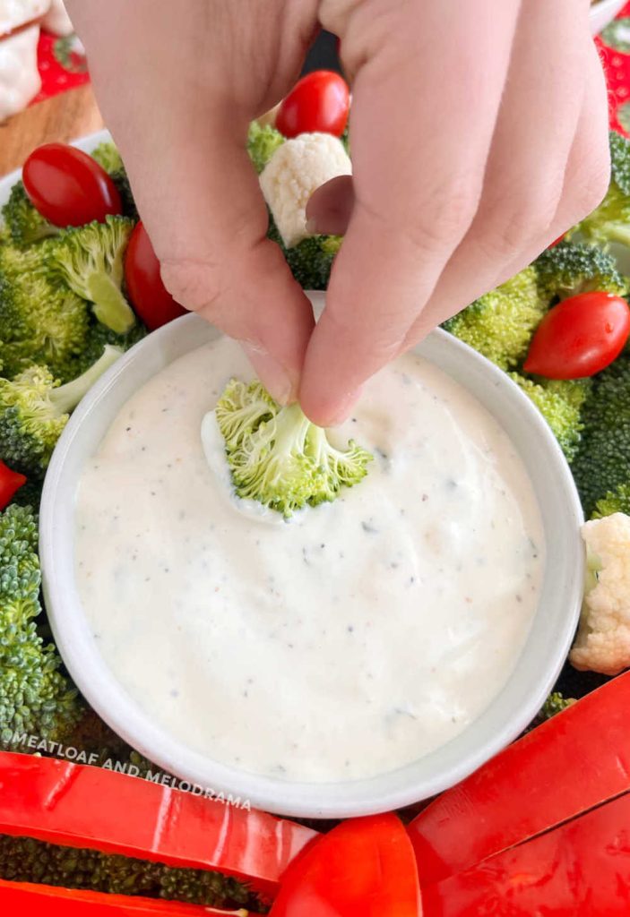 hand dipping raw broccoli in ranch dressing