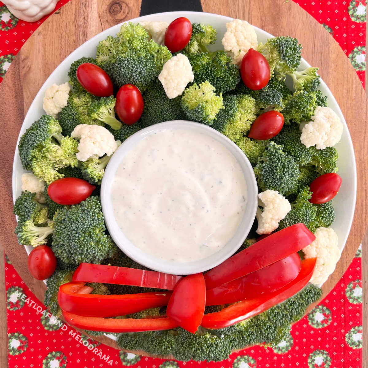 christmas wreath vegetable platter made with broccoli, cauliflower, tomatoes and red pepper strips with dip