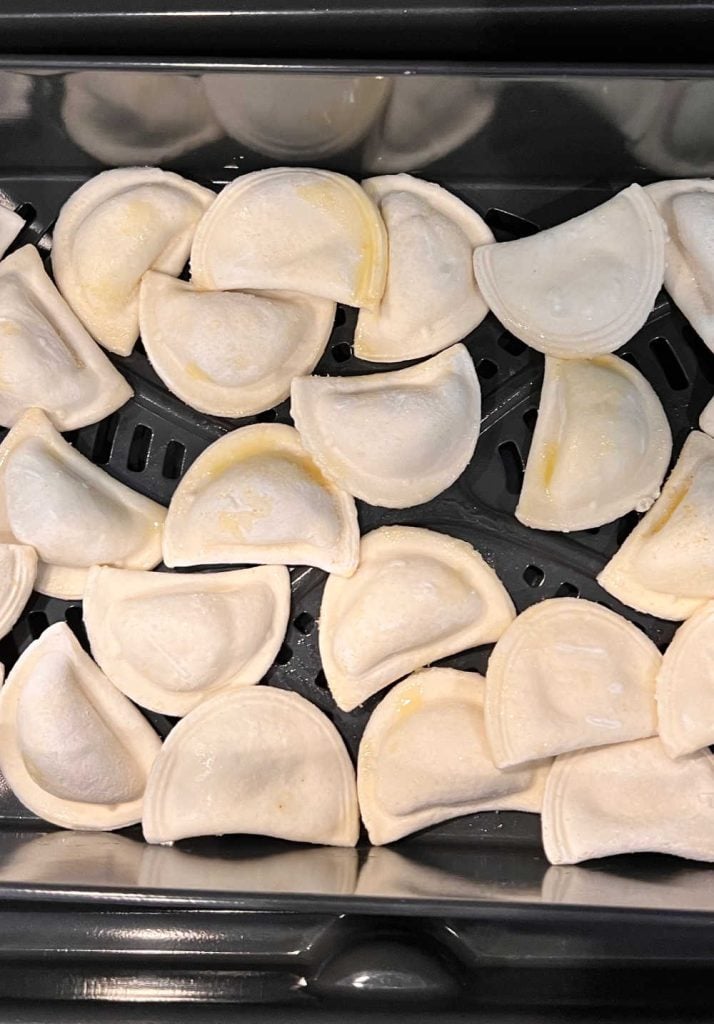 mini frozen pierogies in air fryer tray with olive oil spray