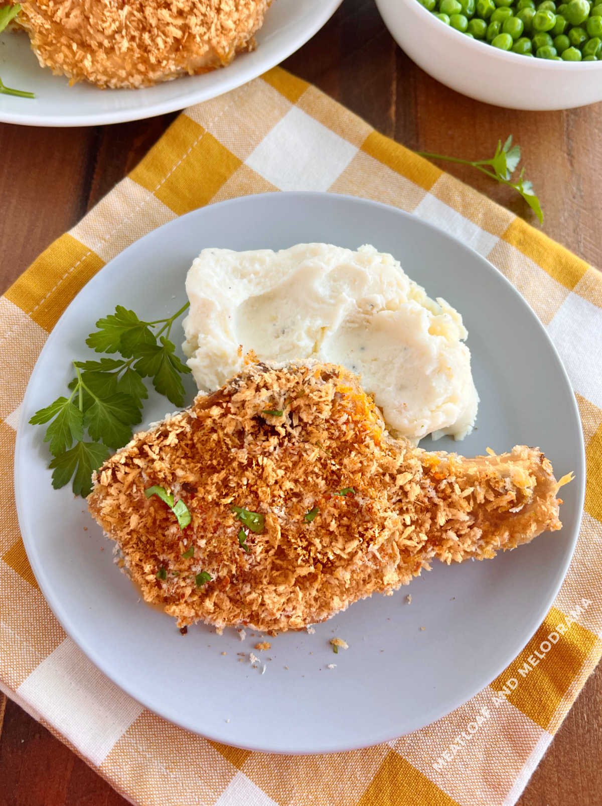 bone-in baked breaded pork chops on the table with mashed potatoes and peas