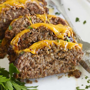 cheesy bbq meatloaf slices with melted cheddar cheese on a white platter