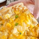 hand holding slice of pierogi pizza (pagach) with cheddar cheese and onions