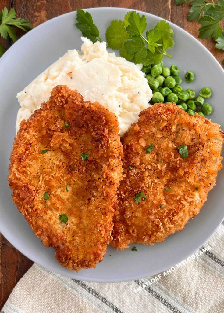 2 polish breaded pork chops with mashed potatoes and peas on table