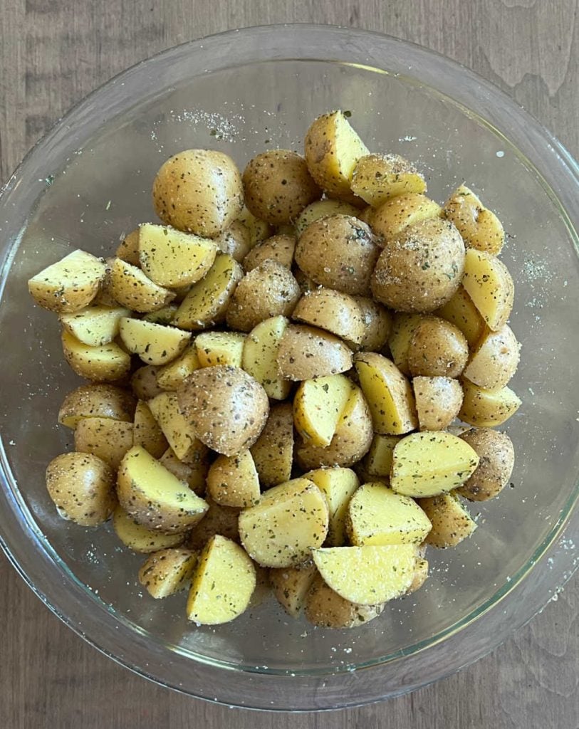 cut baby potatoes with olive oil and spices in glass bowl
