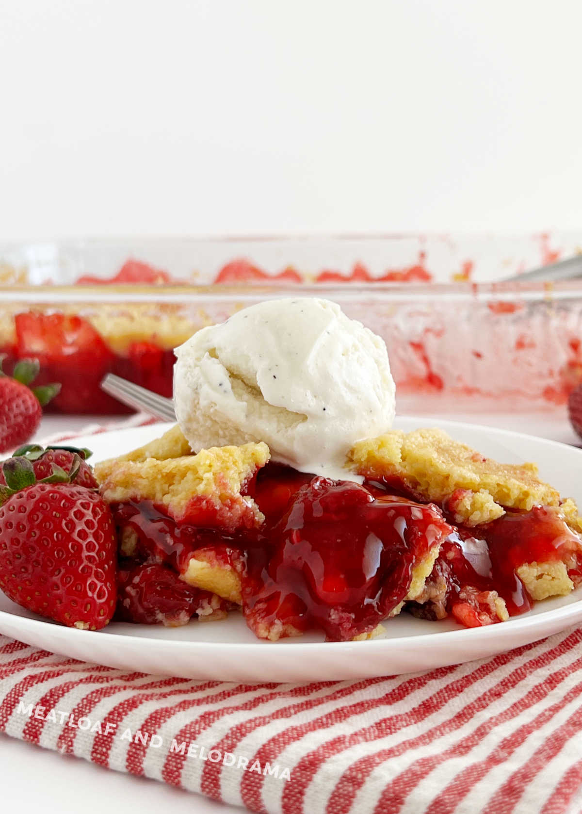 strawberry dump cake on a plate with fresh strawberries and scoop of vanilla ice cream