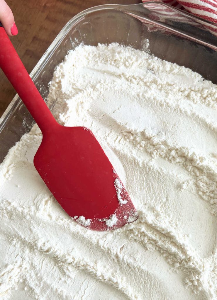 smooth dry cake mix over pie filling in baking pan with red spatula