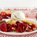 slice of strawberry dump cake with strawberry filling and fresh strawberries and ice cream