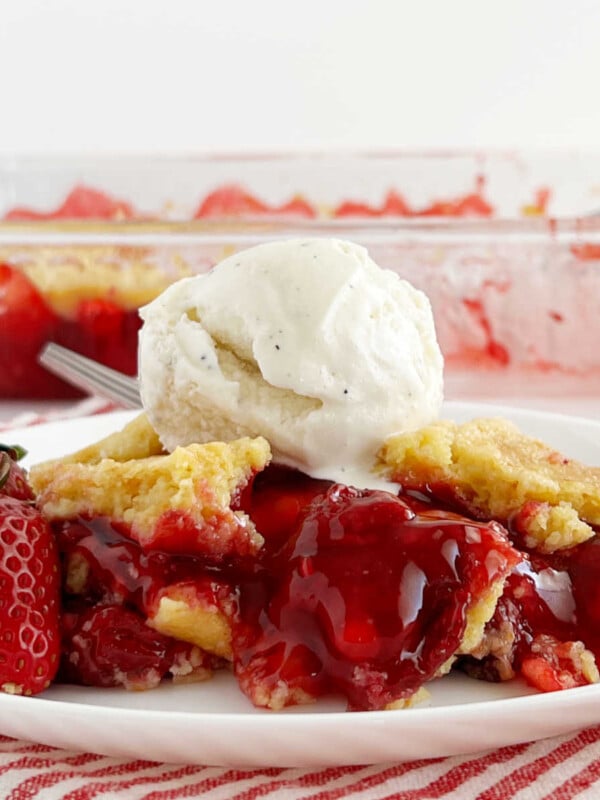 slice of strawberry dump cake with strawberry filling and fresh strawberries and ice cream