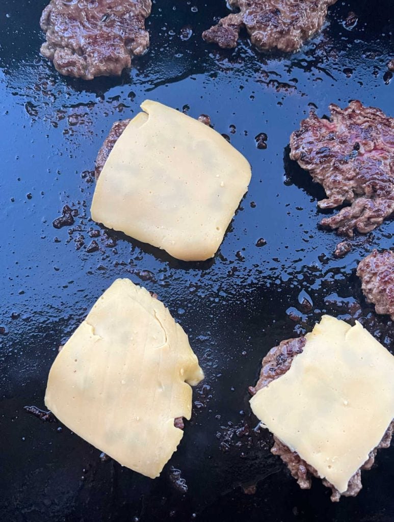 burger patties on blackstone griddle with american cheese slices