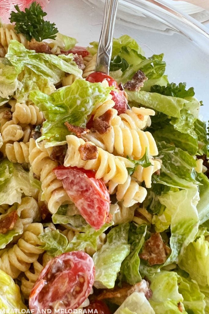 BLT pasta salad with rotini, lettuce and sliced tomatoes on a serving spoon