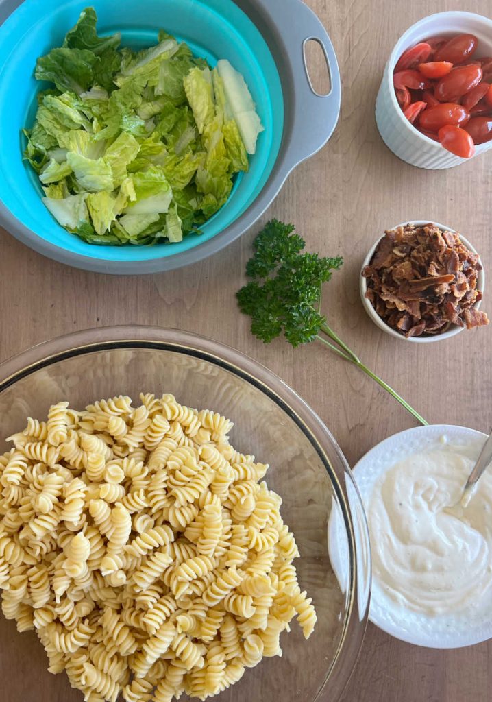 rotini pasta, romaine lettuce, tomatoes, bacon and dressing on the table