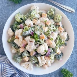 broccoli cauliflower salad with cheese in a creamy dressing in white serving bowl