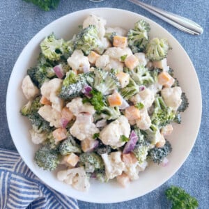 broccoli cauliflower salad with cheese in a creamy dressing in white serving bowl