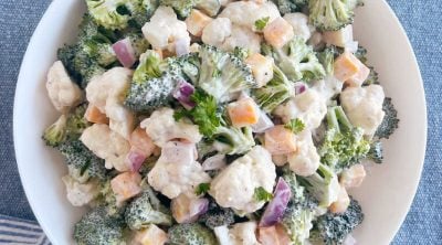 broccoli cauliflower salad with cheese in a creamy dressing in white serving bowl