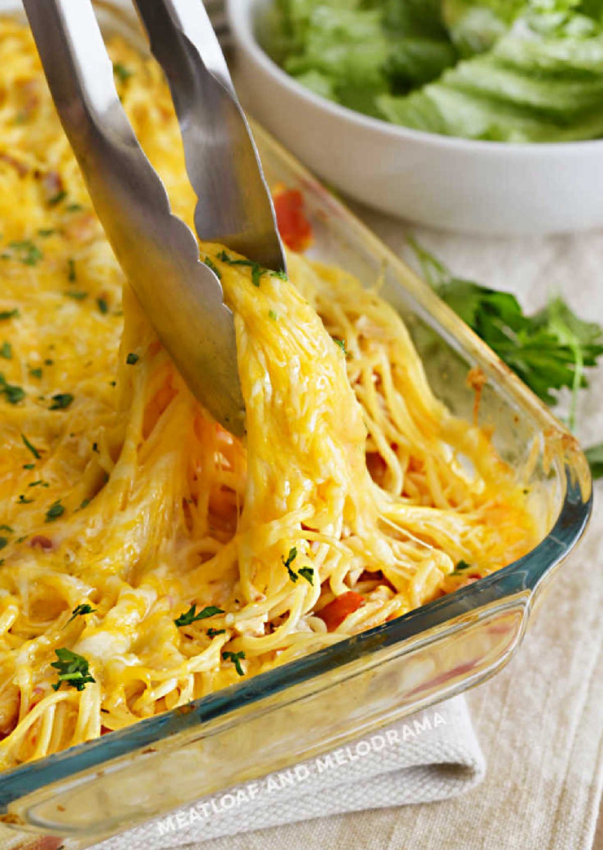 chicken spaghetti with melted cheese in casserole dish with salad