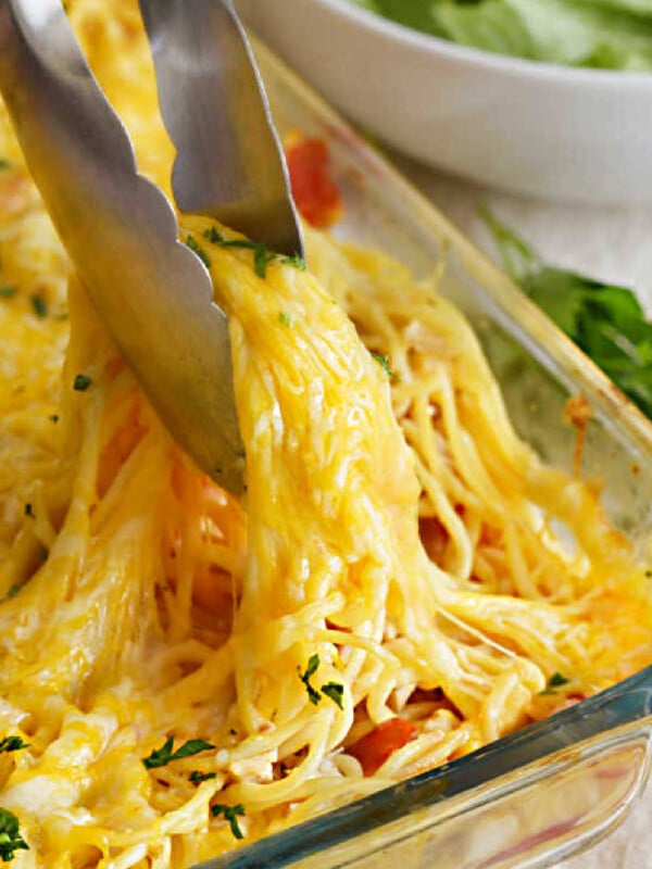 cheesy chicken spaghetti with diced tomatoes in kitchen tongs
