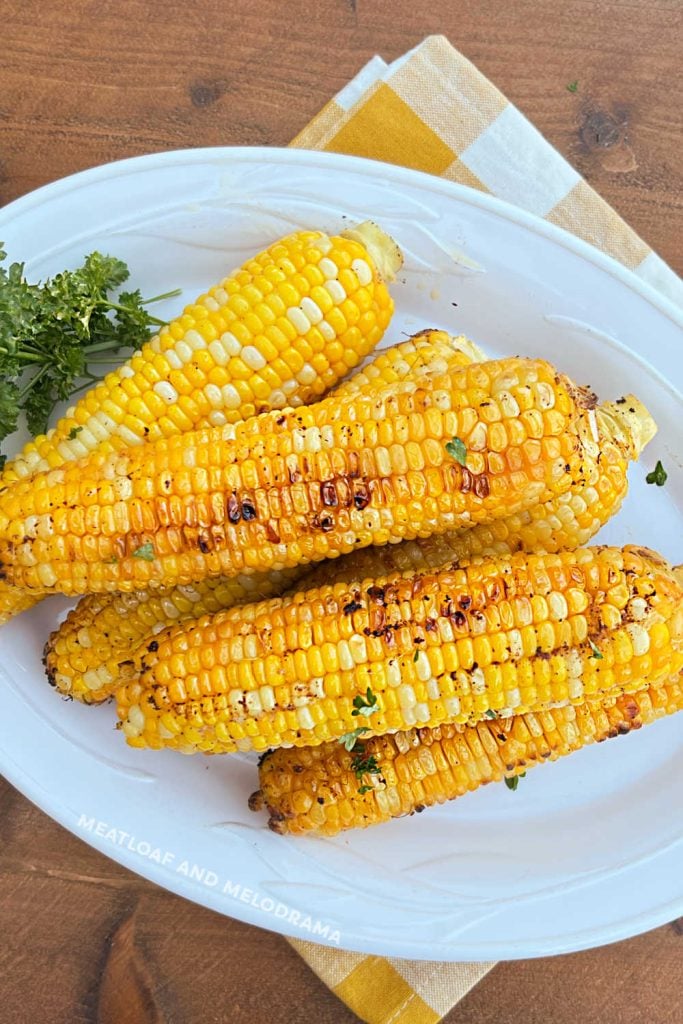 foil grilled corn on a white serving platter with parsley