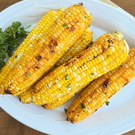 grilled corn on the cob in foil with parsley on platter