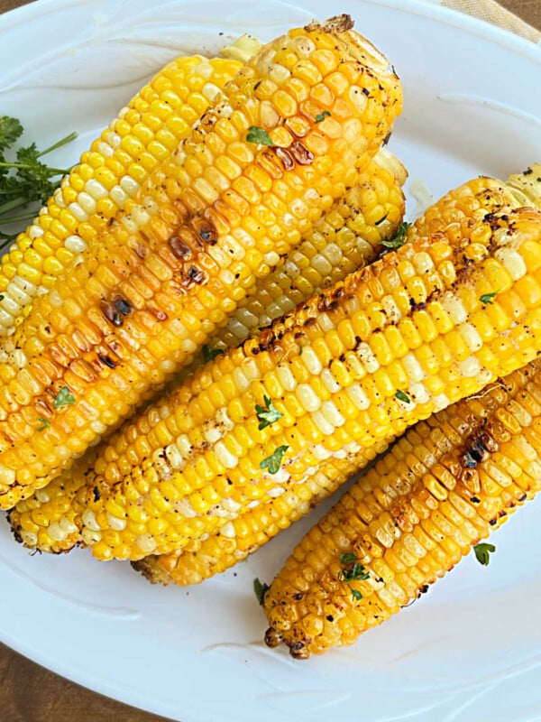 grilled corn on the cob in foil with parsley on platter