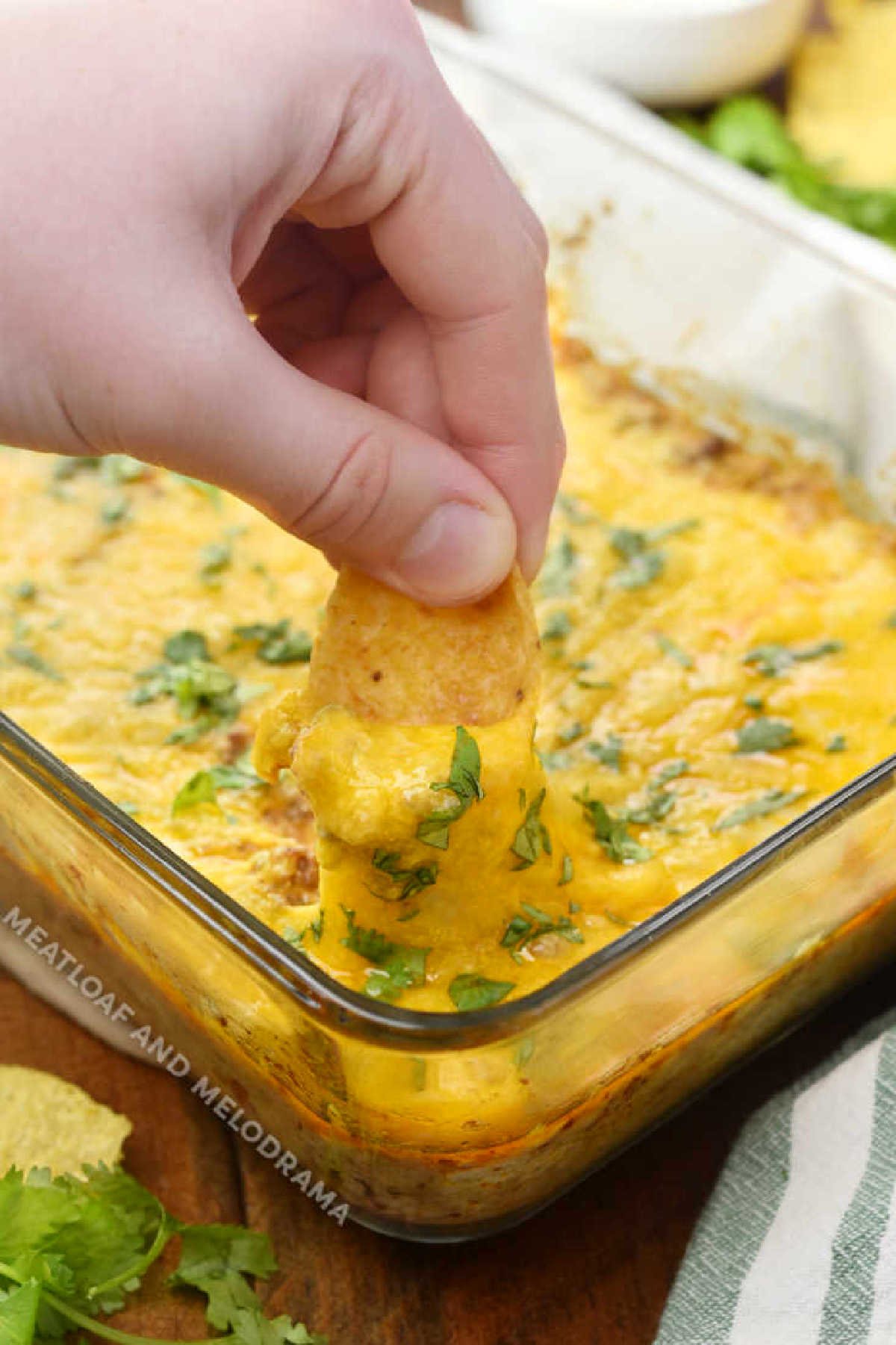 dip frito chip into baked taco dip with ground beef and cheese
