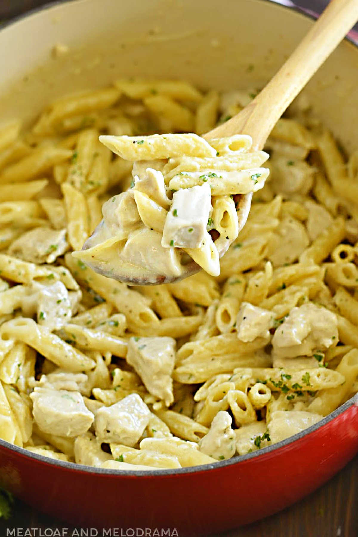 one pot chicken alfredo penne pasta on wooden spoon in dutch oven