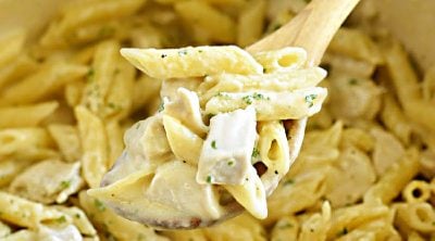 chicken alfredo penne pasta on wooden spoon over Dutch oven
