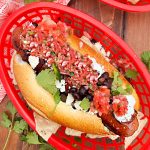sonoran hot dog with bacon, black beans, cotija cheese and salsa on bolillo roll on table
