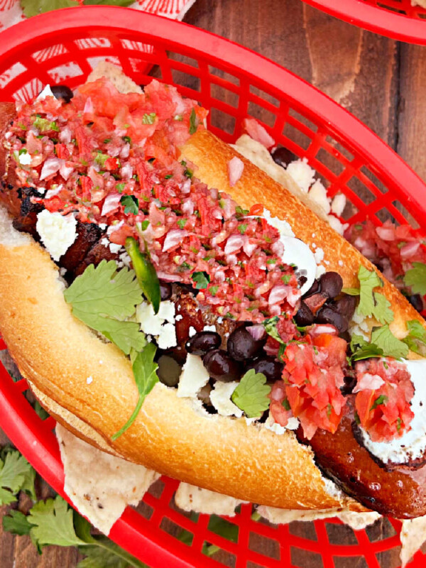sonoran hot dog with bacon, black beans, cotija cheese and salsa on bolillo roll on table