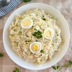 grandma's potato salad with red potatoes, eggs and parsley in a white serving bowl