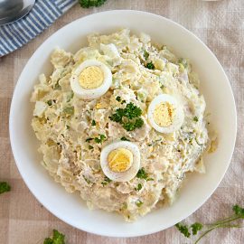 grandma's potato salad with red potatoes, eggs and parsley in a white serving bowl