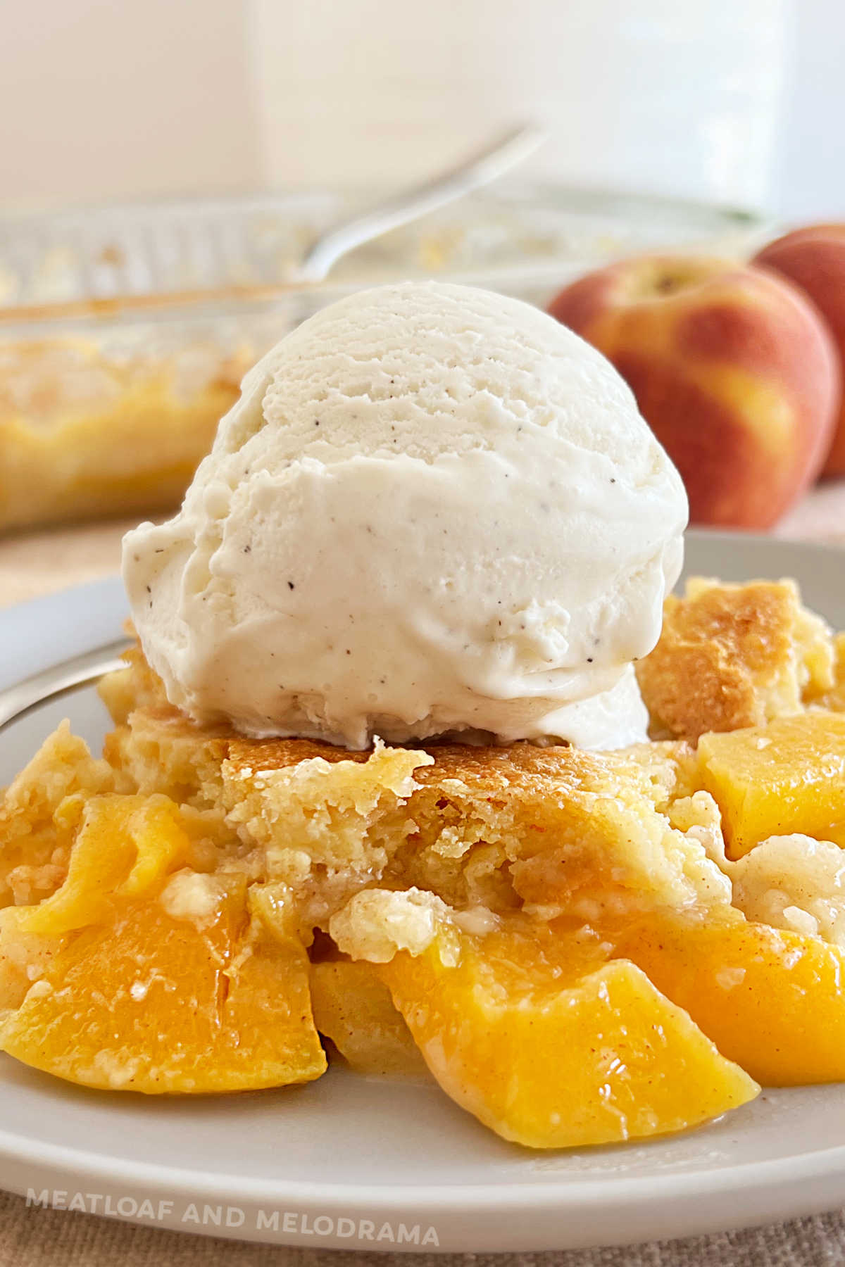 peach dump cake with scoop of vanilla ice cream on top and fresh peaches in back