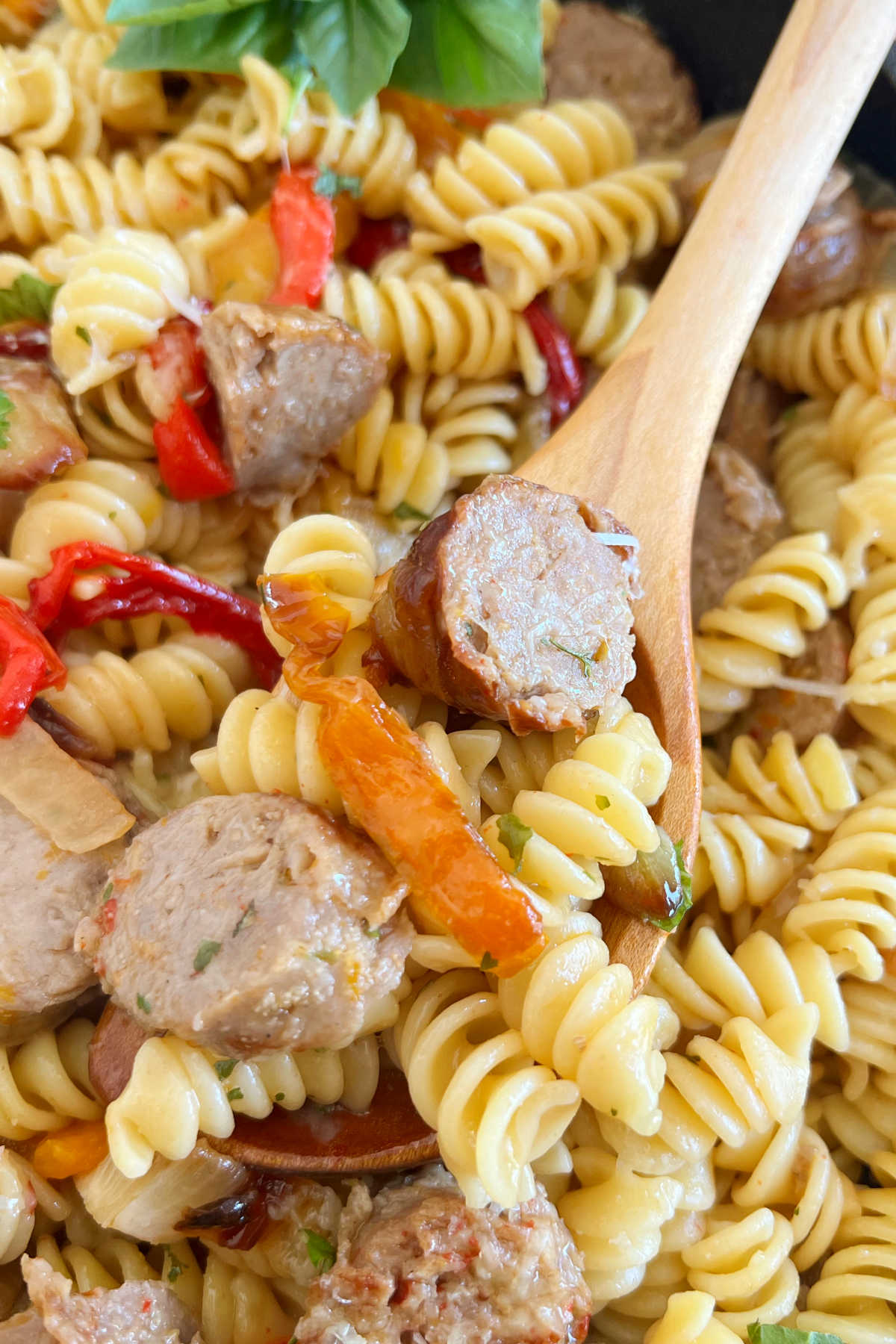 italian sausage and peppers pasta on a wooden spoon