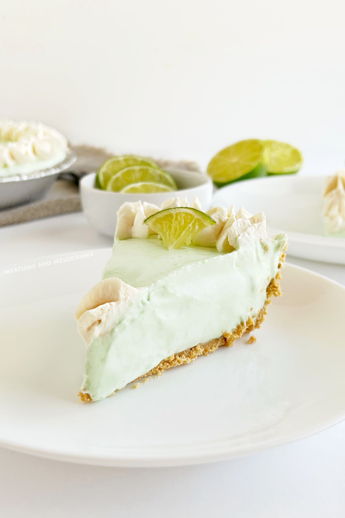 slice of no bake key lime pie on graham cracker crust with limes on plate