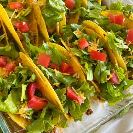 crispy oven baked tacos with ground beef, cheese, lettuce and tomatoes in baking dish