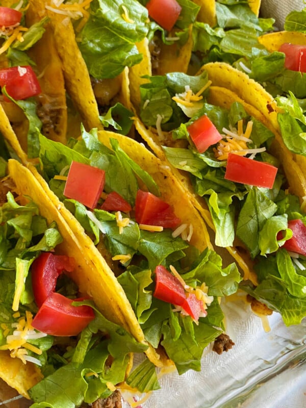 crispy oven baked tacos with ground beef, cheese, lettuce and tomatoes in baking dish
