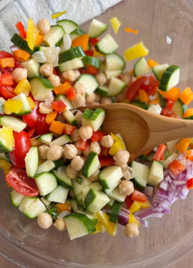 mix garbanzo beans and salad ingredients with wooden spoon