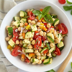 simple chickpea salad with cucumbers, red onion, tomatoes and bell peppers in white bowl