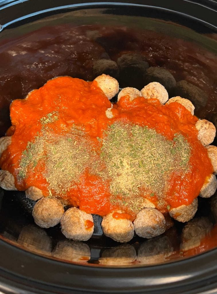 frozen meatballs covered with marinara sauce and herbs in slow cooker