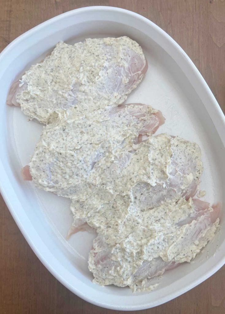 chicken breasts coated with mayonnaise in baking dish