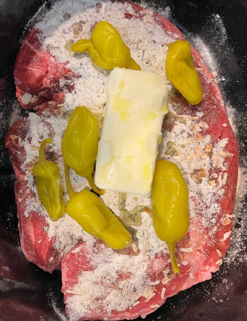 boneless chuck roast topped with dry ranch dressing, onion soup mix, butter and peperoncini peppers in crock pot