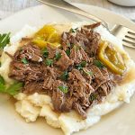 shredded crock pot Mississippi pot roast with peperoncini peppers over mashed potatoes