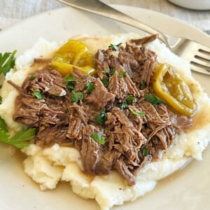 shredded crock pot Mississippi pot roast with peperoncini peppers over mashed potatoes