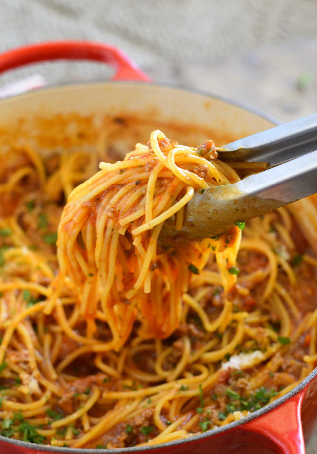 one-pot spaghetti in red Dutch oven with kitchen tongs