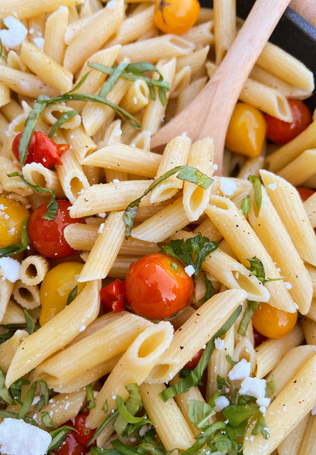 penne pasta and garden fresh cherry tomatoes and basil in wooden spoon