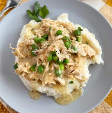 crockpot chicken and gravy over mashed potatoes and peas on a blue plate