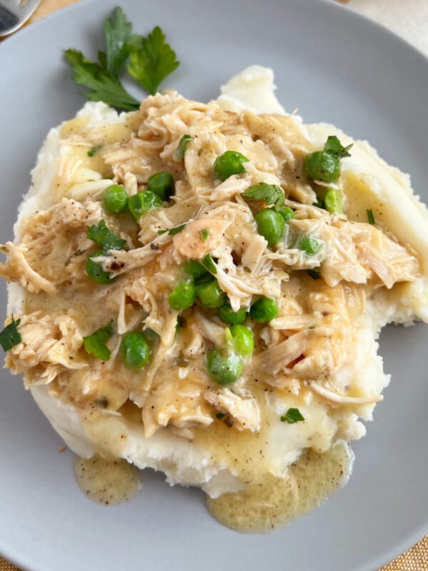 crockpot chicken and gravy over mashed potatoes and peas on a blue plate