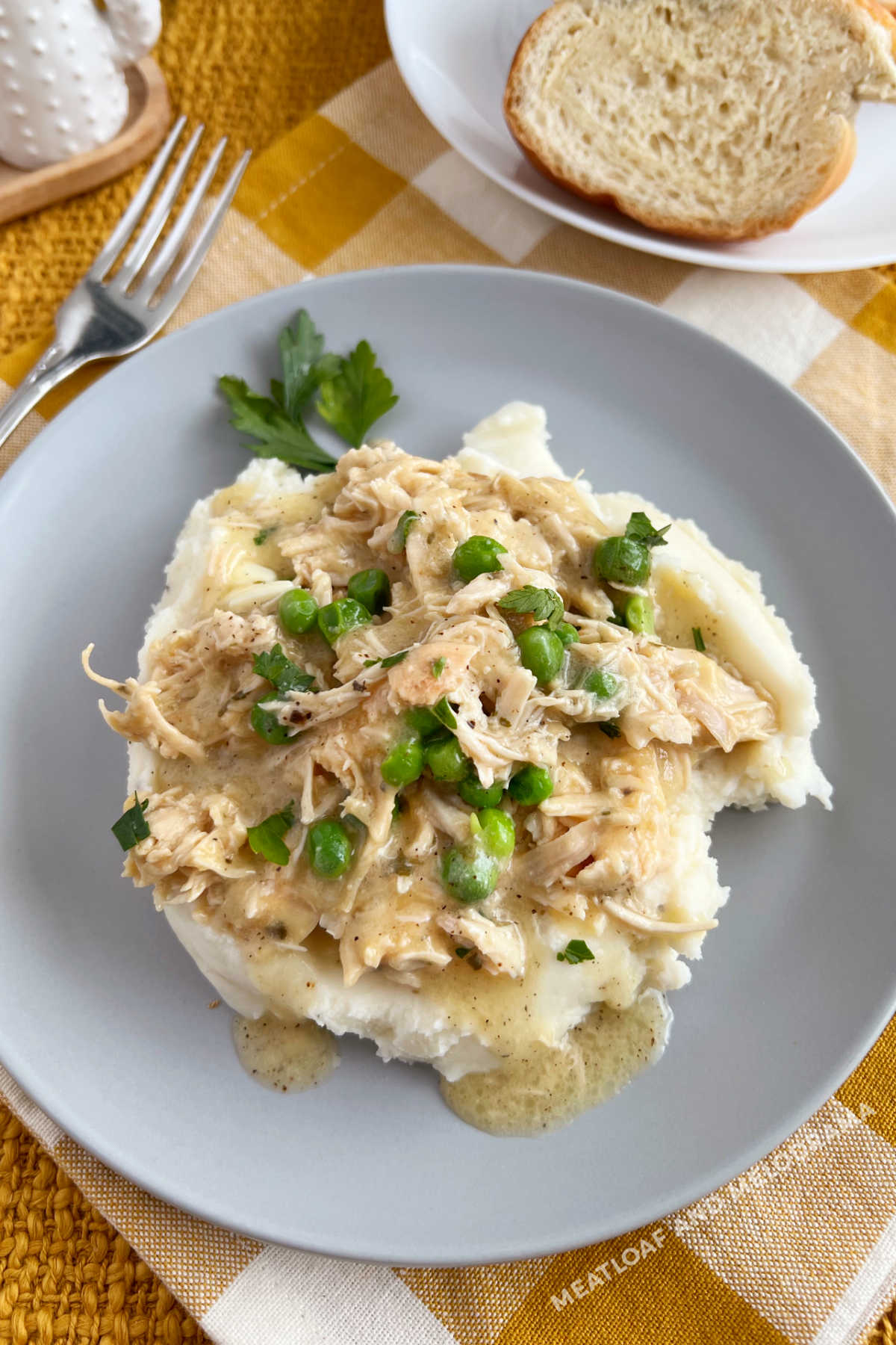 crockpot chicken and gravy over mashed potatoes with peas on the table