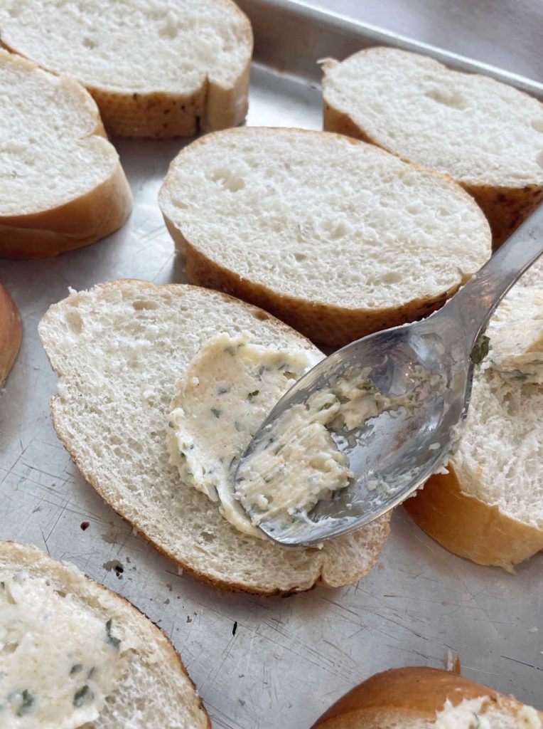 spread garlic butter on bread slices with spoon
