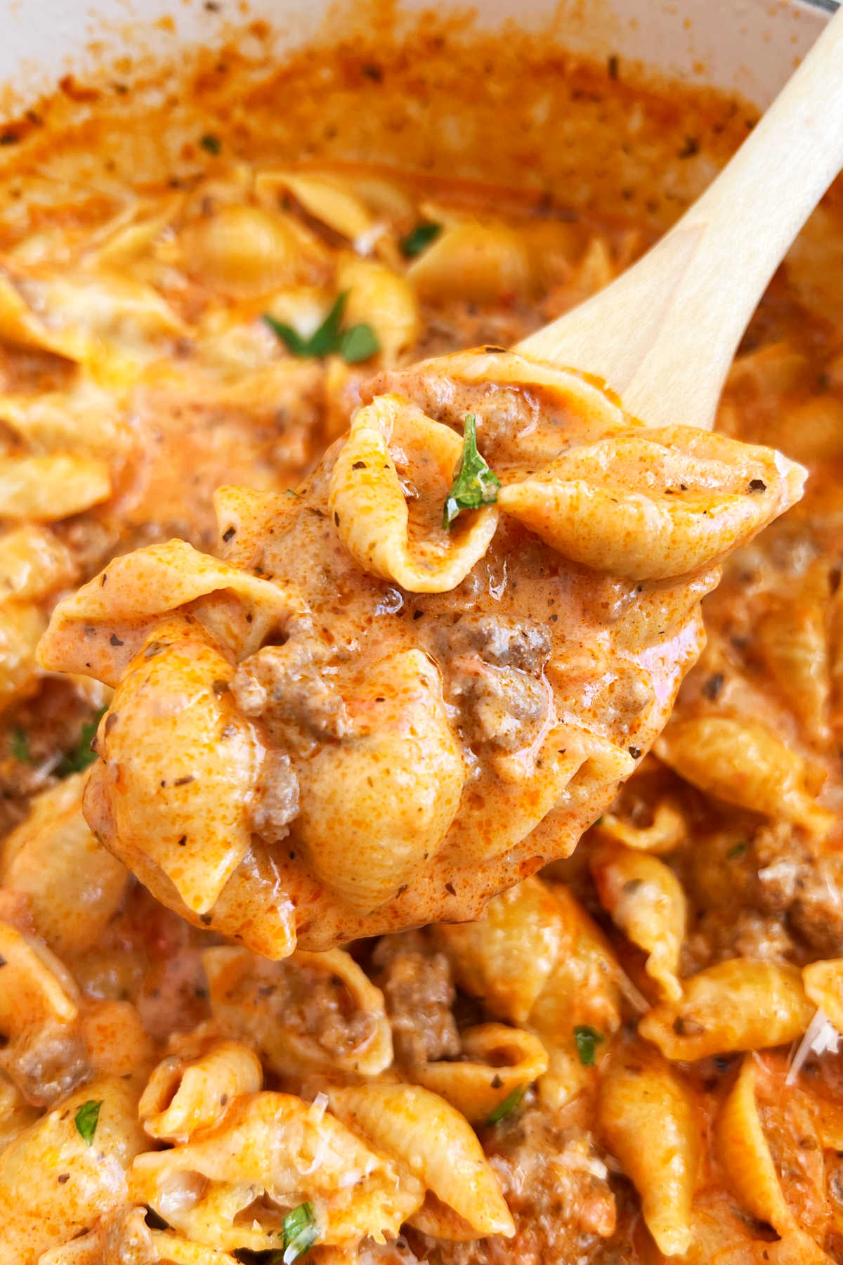 creamy shells and beef in tomato sauce on wooden spoon