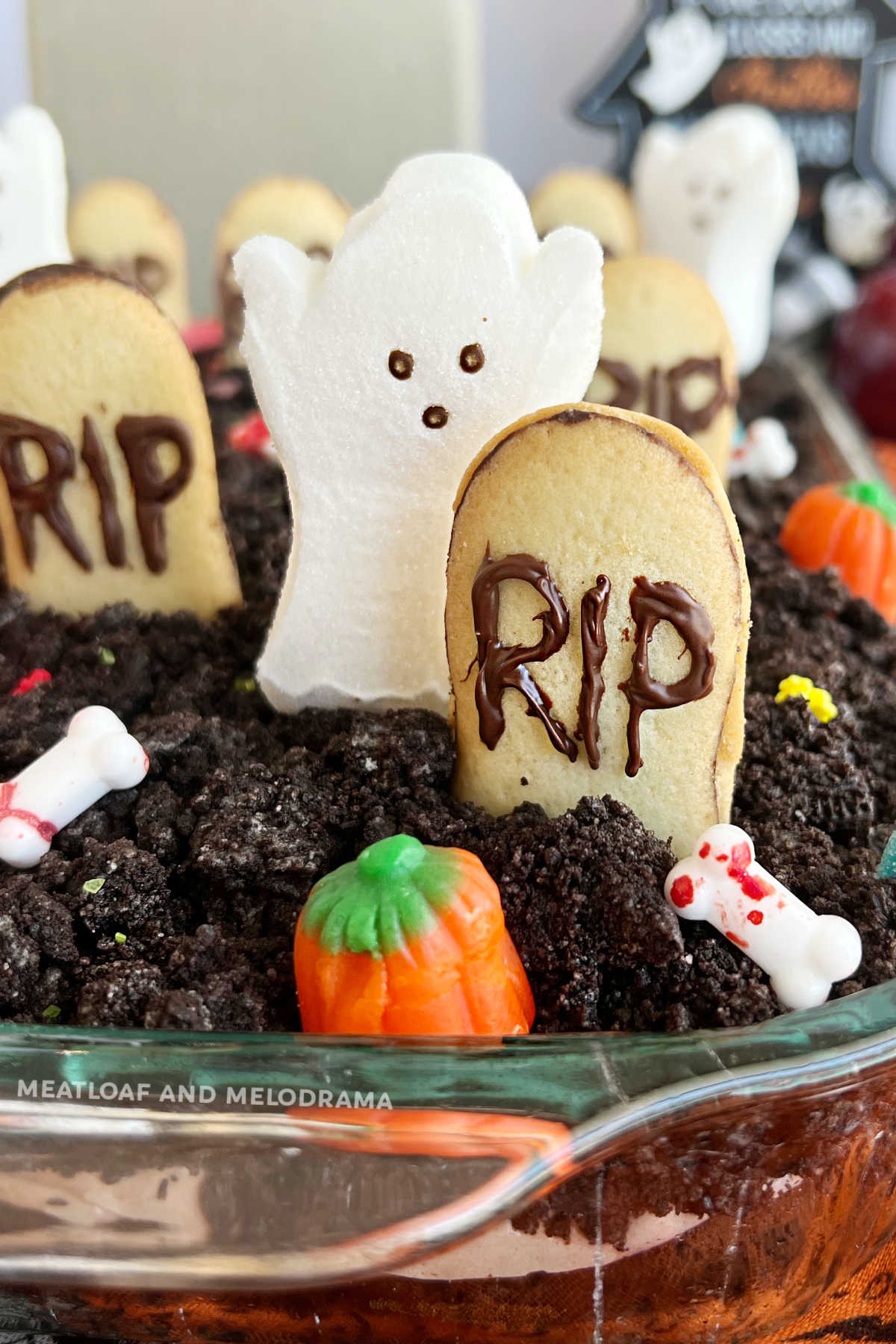 halloween dirt cake (graveyard cake) with ghost, pumpkins, gummy worms and gravestones in baking dish.